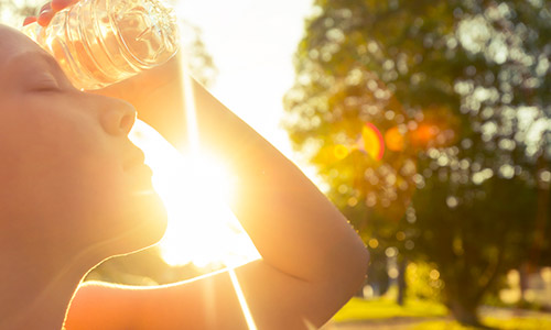 woman holding water bottle on forehead during hot day